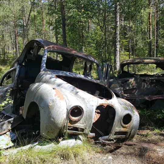 En gammal rostig bil utan hjul som står i grönska